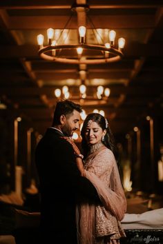 a man and woman standing in front of a chandelier with lights on the ceiling