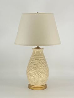 a table lamp with a white shade on the top and gold trim around the base