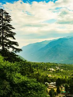 the mountains are covered with trees and houses in the valley below, under a cloudy blue sky