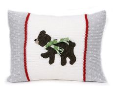 a knitted pillow with a teddy bear on the front and green ribbon around the neck