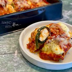 a white plate topped with lasagna covered in sauce next to a casserole dish