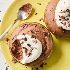 two desserts with whipped cream and chocolate shavings on yellow plate next to spoon