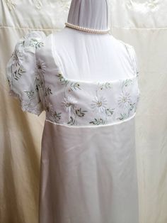 This dress has free standard shipping included!  Standard shipping Air Mail, no tracking.  If you would like Express Post or place by place tracking, please contact us, and we can set that up for you!   We offer a basic Regency styled gown, with the empire waist and short puffed sleeves.  This dress is made with a solid white satin skirt, and an overlay of daisies on the top.  The sleeves have been trimmed with white lace.    *This gown ties at the back with ribbons which can adjust the fit.  Dr White Fitted Empire Waist Vintage Dress, White Fitted Vintage Dress With Empire Waist, White Regency Gown With Fitted Bodice, White Regency Style Gown With Fitted Bodice, Fitted White Victorian Dress With Short Sleeves, White Fitted Gown With Empire Waist, Fitted Short Sleeve Regency Style Dresses, Regency Style Fitted Dress With Square Neck, Regency Style Fitted Empire Waist Dress