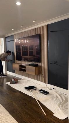 a man standing in front of a flat screen tv next to a wooden table with paint on it