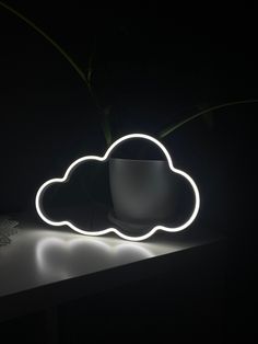 a white cloud shaped light sitting on top of a table next to a cup and plant