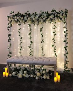 a bench with candles and flowers on it in front of a curtained wall decorated with lights