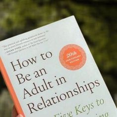 the book how to be an adult in relationships is being held up by someone's hand