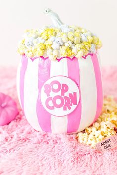 a pink and white striped popcorn bucket with pop corn in it on a pink carpet