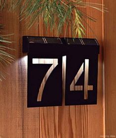 a house number sign mounted to the side of a wooden wall next to a pine tree