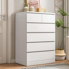 a white chest of drawers in a living room next to a potted plant and door