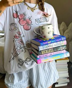 a woman holding a stack of books and a coffee mug in her hand while wearing pajamas