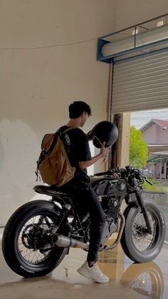 a man sitting on top of a motorcycle holding a helmet in his hand and looking at the ground