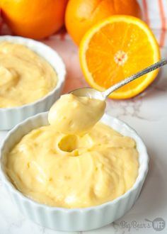 an orange being spooned into two small bowls filled with cheesecake batter and surrounded by oranges