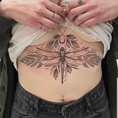 a woman's stomach with a dragonfly tattoo on the side and leaves around it