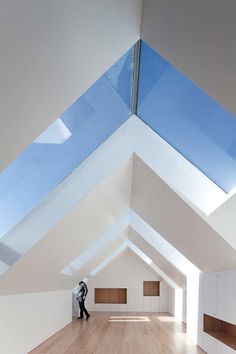 an empty room with wooden floors and skylights on the ceiling, while a person is standing in the doorway