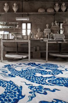 a large rug with blue and white designs on the floor in a room filled with vases