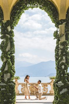 a man and woman standing in front of an archway with vines on the sides, looking at each other