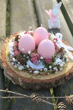 three pink eggs sitting on top of a piece of wood next to some pine cones