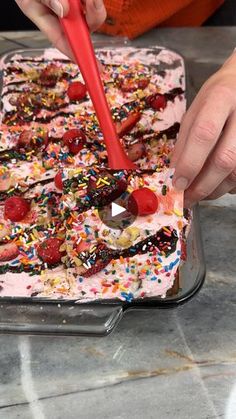 a person cutting into a cake with sprinkles and cherries on it