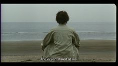 a woman standing on top of a sandy beach next to the ocean in front of an overcast sky