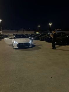 a man standing next to a white sports car in a parking lot with other cars