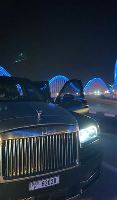 two rolls royces are parked in front of a bridge at night with the lights on