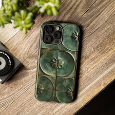 a cell phone case sitting on top of a wooden table next to a camera and plant