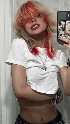 a woman with red hair and piercings is holding up her cell phone to take a selfie