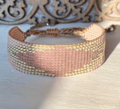 a pink and gold bracelet sitting on top of a wooden table next to a wall