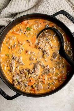 a pot filled with meat and vegetable soup on top of a white table next to a gray towel