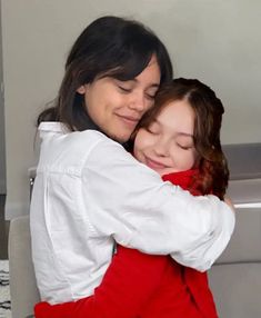 two women hugging each other in front of a white refrigerator freezer with the door open