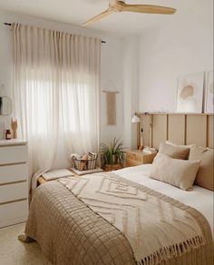 a bed room with a neatly made bed and a ceiling fan in the corner next to a window