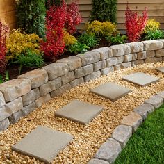 a stone wall with stepping stones in front of it and colorful flowers around the edges