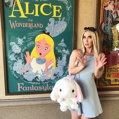 a woman is holding a stuffed animal in front of a book cover with an image of alice on it