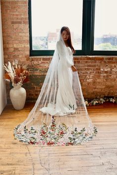 a woman standing in front of a window wearing a wedding dress with a long veil