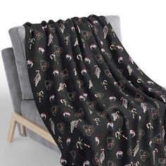 a black blanket with white cats on it sitting on a grey couch next to a wooden frame