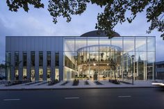 a large glass building sitting on the side of a road next to a tree filled street