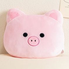 a pink stuffed pig pillow sitting on top of a bed next to a white wall