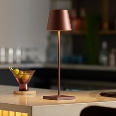 a table lamp sitting on top of a white counter next to a bowl of fruit