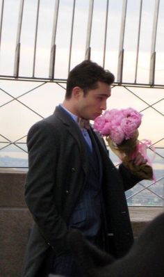 a man in a suit and tie holding pink flowers on top of the empire building