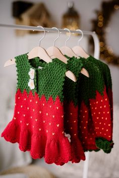 two knitted strawberry sweaters hanging on a clothes rack in front of a bed