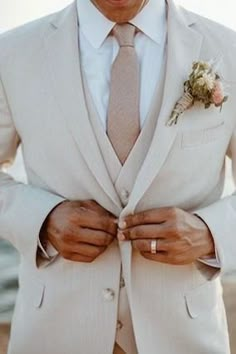 a man in a white suit and tie with his hands on his lapel pocket