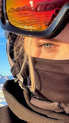 a woman wearing ski goggles and a scarf on top of her head with mountains in the background