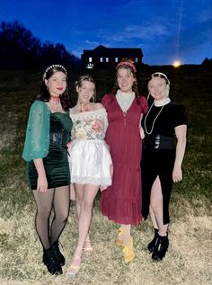 four women dressed up in costumes posing for a photo at night with the sky behind them