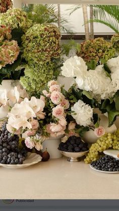 there are many different types of flowers in bowls on the counter top with grapes and grapes