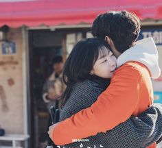 a man and woman embracing each other in front of a building with red awnings