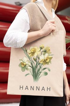 a woman carrying a tan tote bag with yellow flowers on it and the words hannah