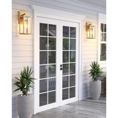 two potted plants sitting on the side of a white house next to an open patio door