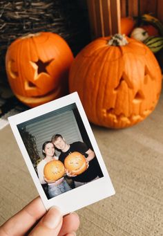 a person holding two pumpkins in front of some jack - o'- lanterns