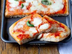 two slices of pizza sitting on top of a black tray next to a knife and fork